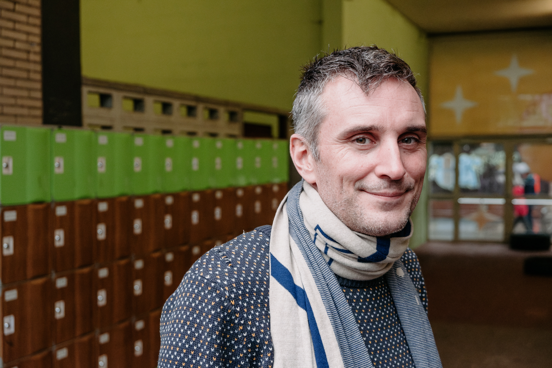 A head-and-shoulders portrait of a man with short gray hair wearing a sweater and scarf.