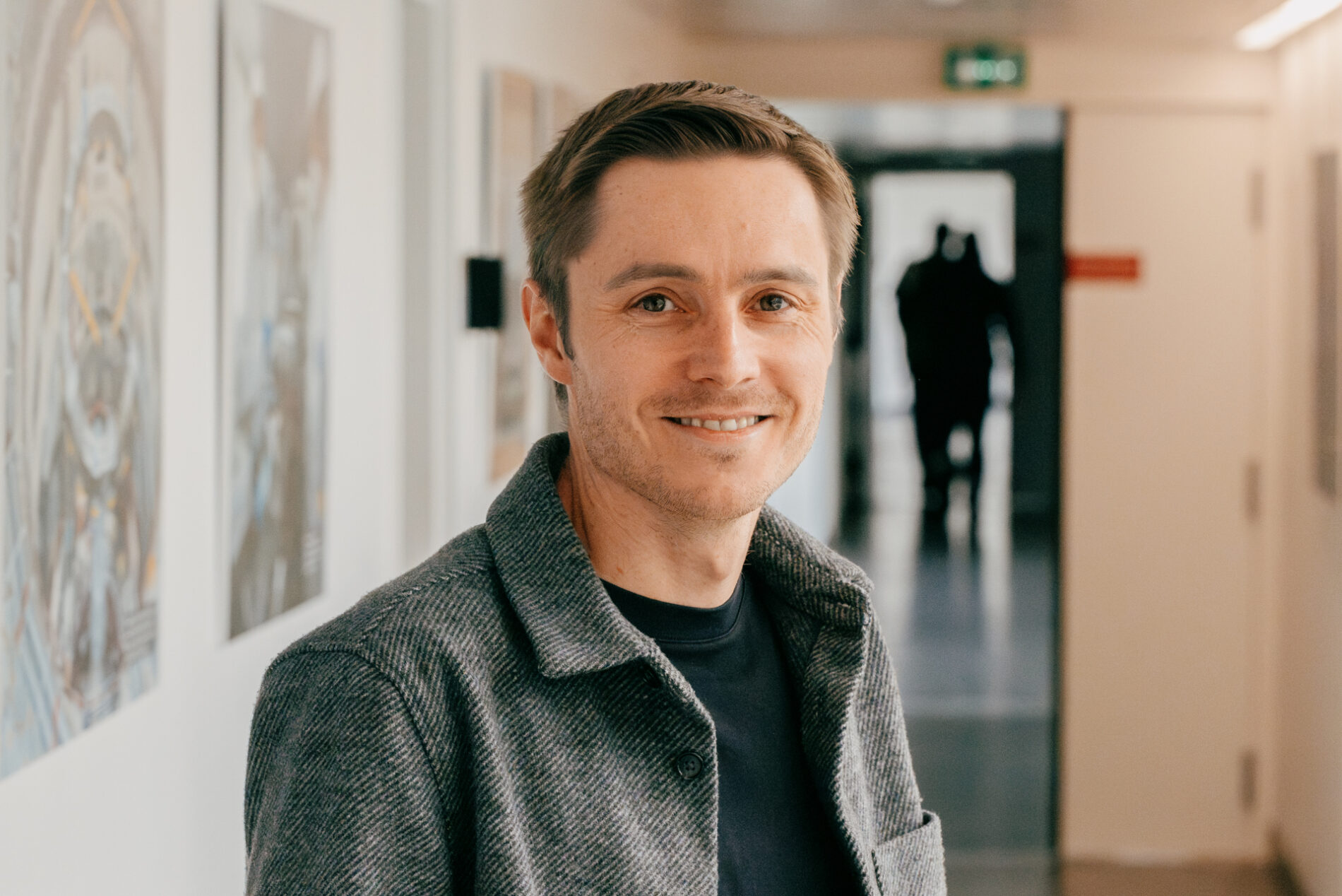 Portrait showing smiling man in a hallway, from the shoulders up, looking directly at the camera.