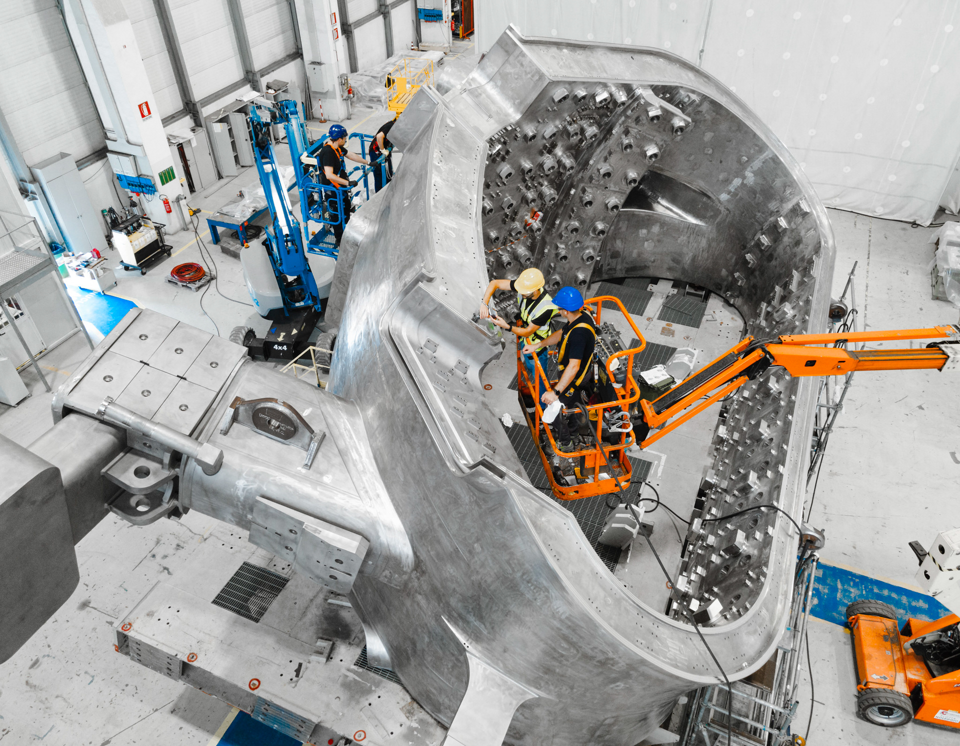 A large ovoid metallic structure with a construction worker on a lift inside it.