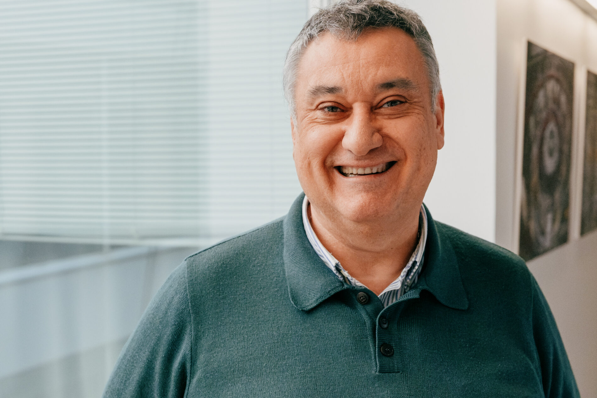 Smiling man in a green sweater in a brightly lit hallway.