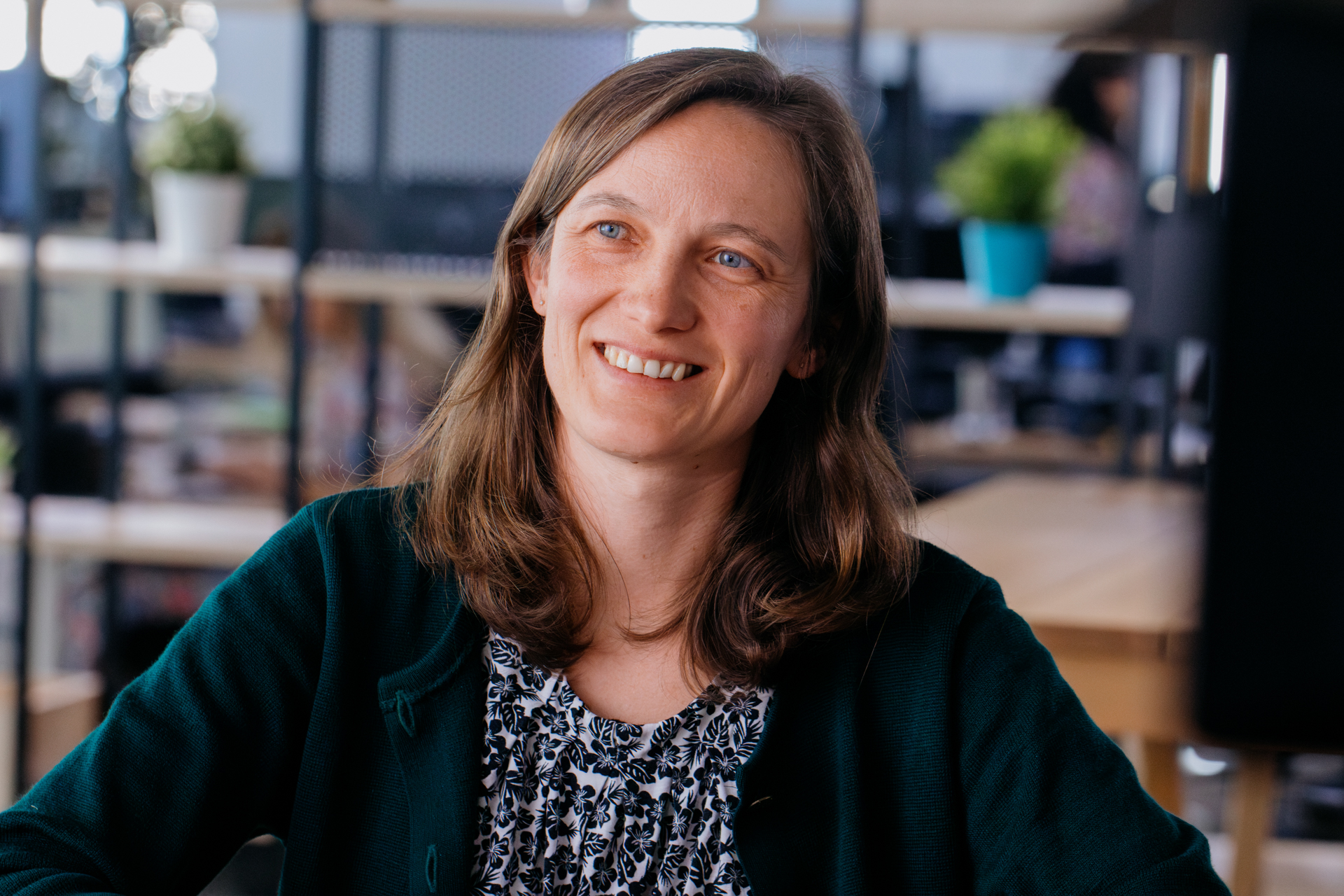 A smiling woman with light brown hair seen face-on sitting at a table.