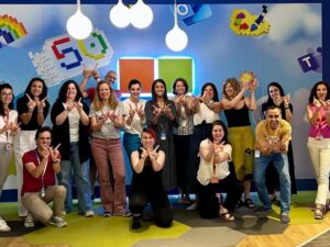 Grupo de personas posando en una foto grupal delante de una pared tematizada con el 50 aniversario de Microsoft