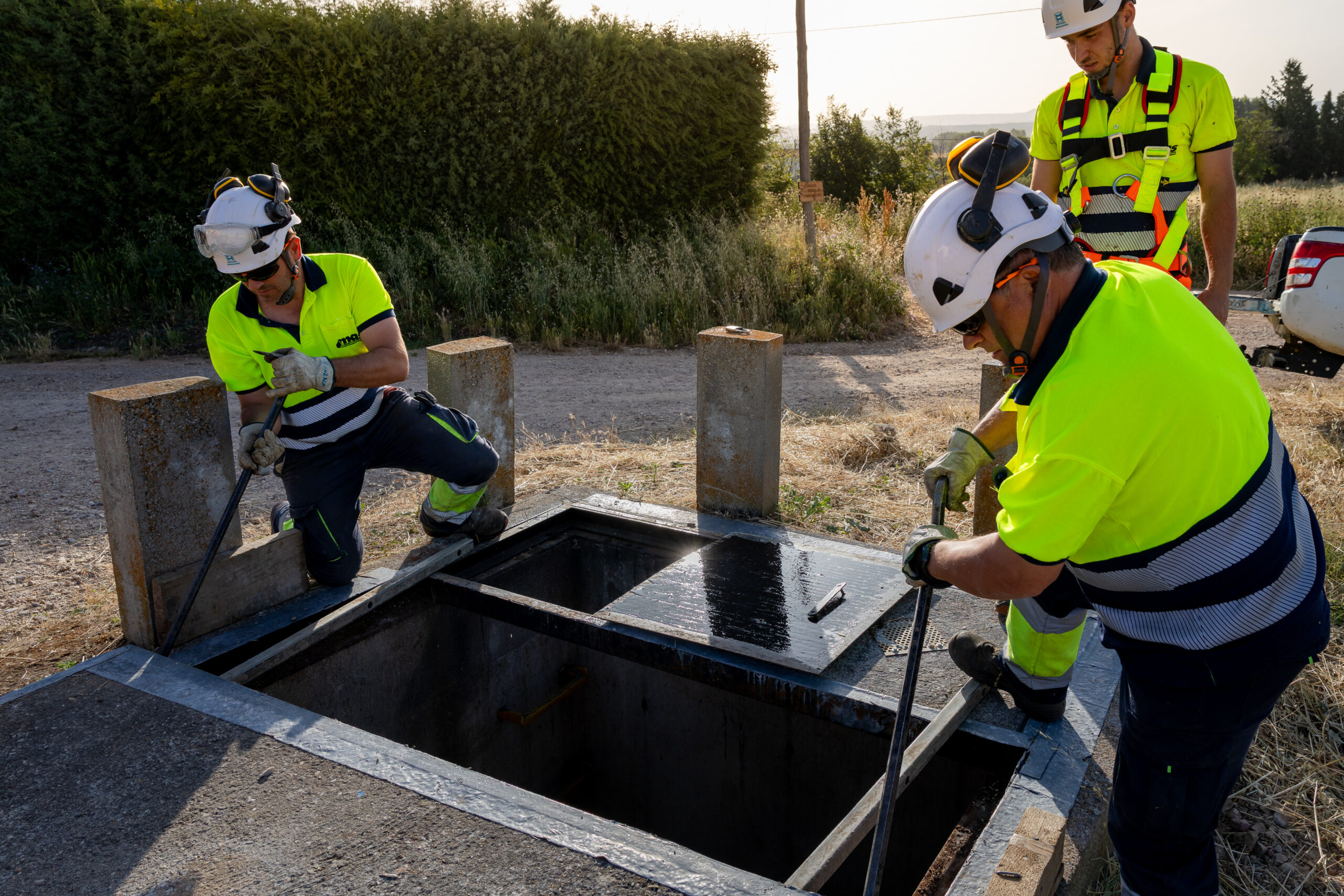 Tres operarios trabajando levantando una tapa del suelo para acceder a las tuberías