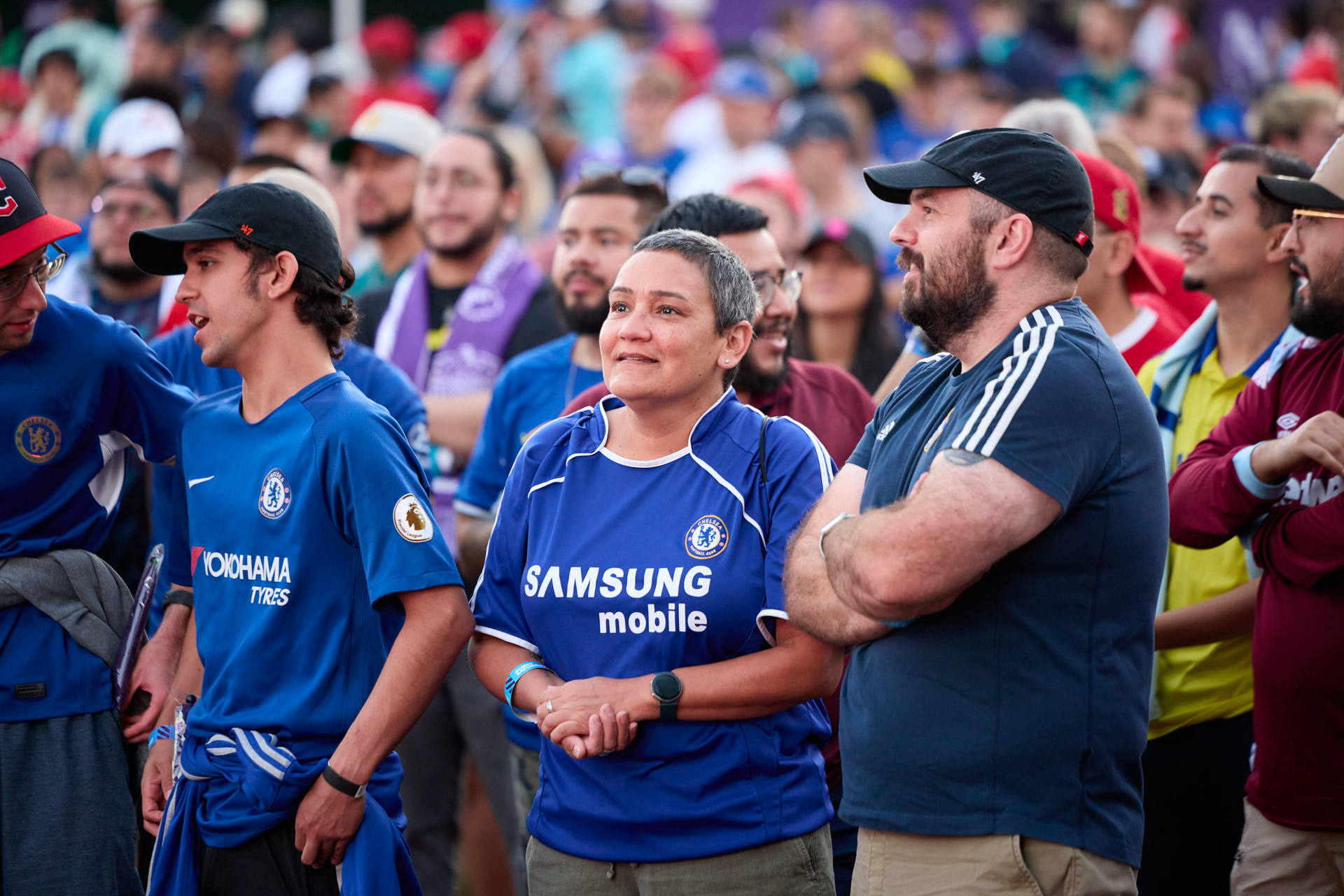 Group of fans gathered at an outdoor event. Three are wearing Chelsea jerseys.