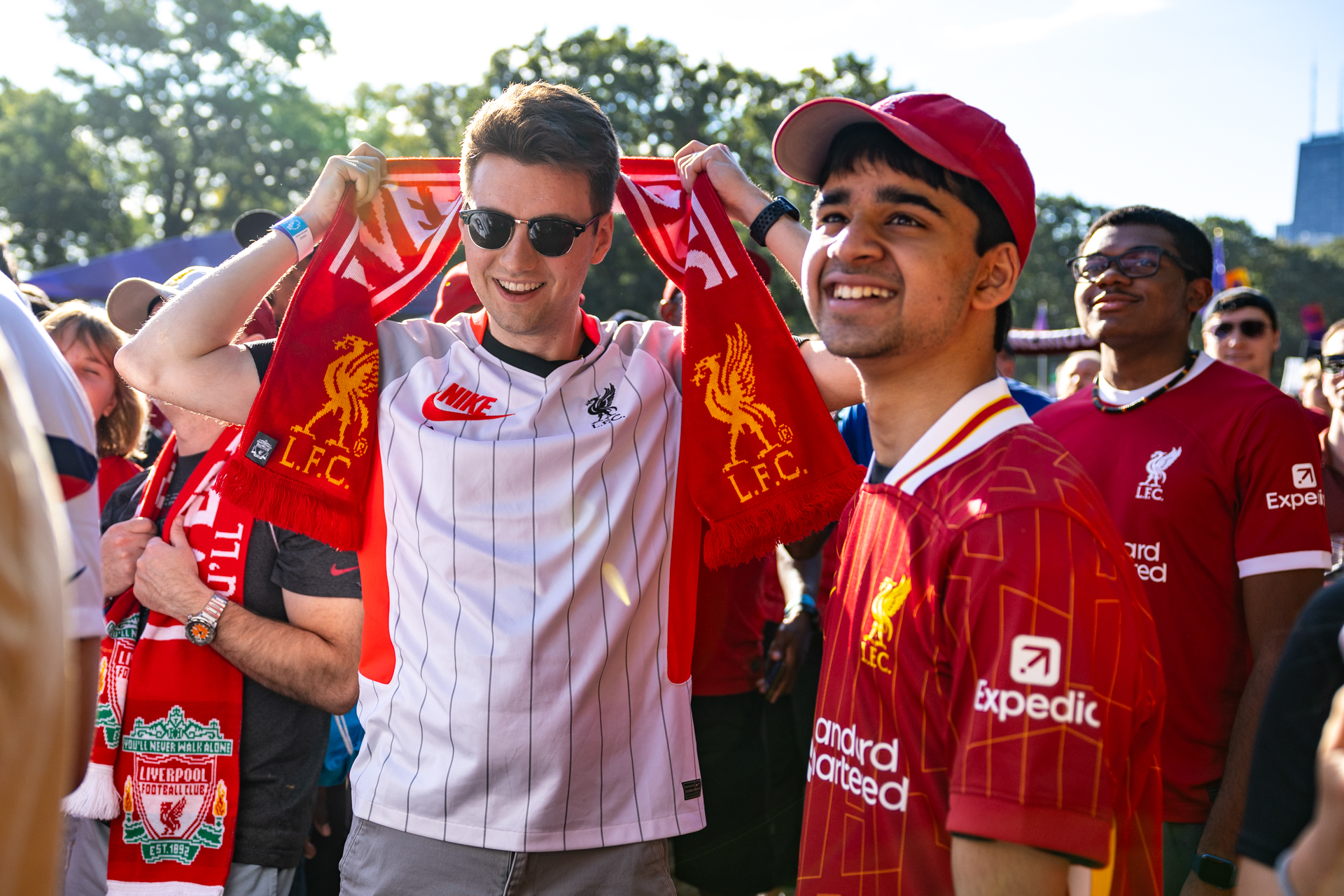 Two Liverpool fans look in the distance. One is wearing a scarf and the other a red hat.