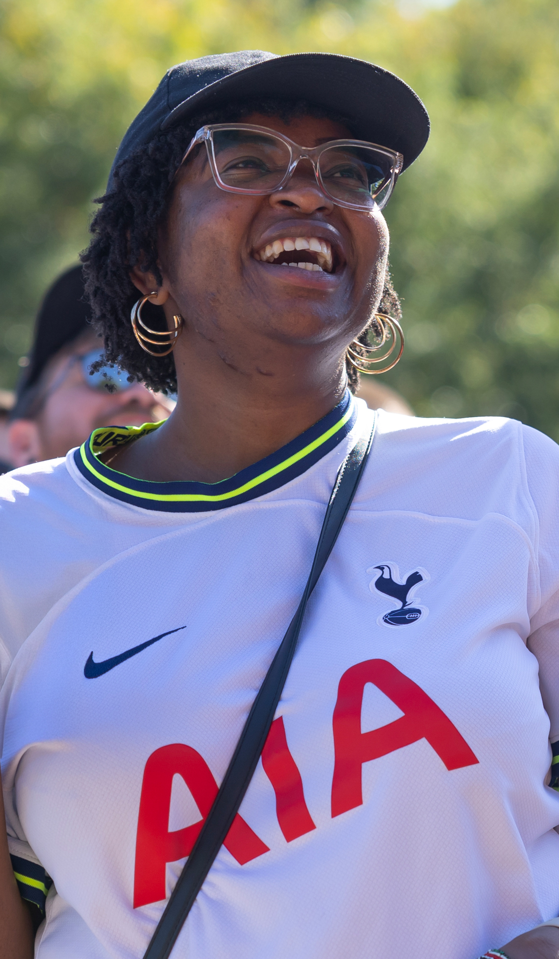 A smiling woman wears a white Tottenham jersey with AIA across the front.
