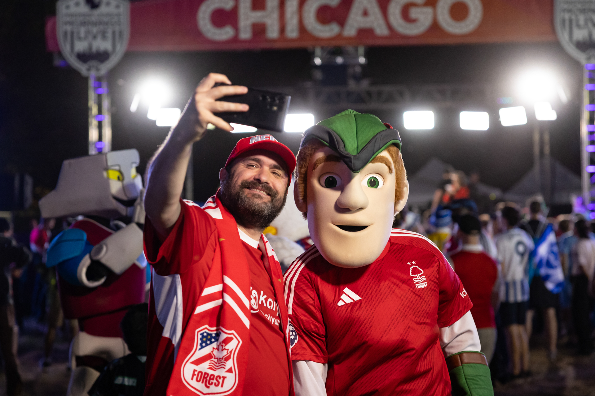 A man wearing a red Nottingham Forest jersey poses with the team’s mascot with a Chicago banner in the background.